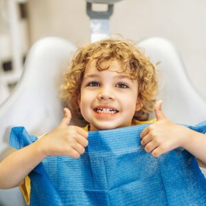 A child at the dentist giving two thumbs up and smiling