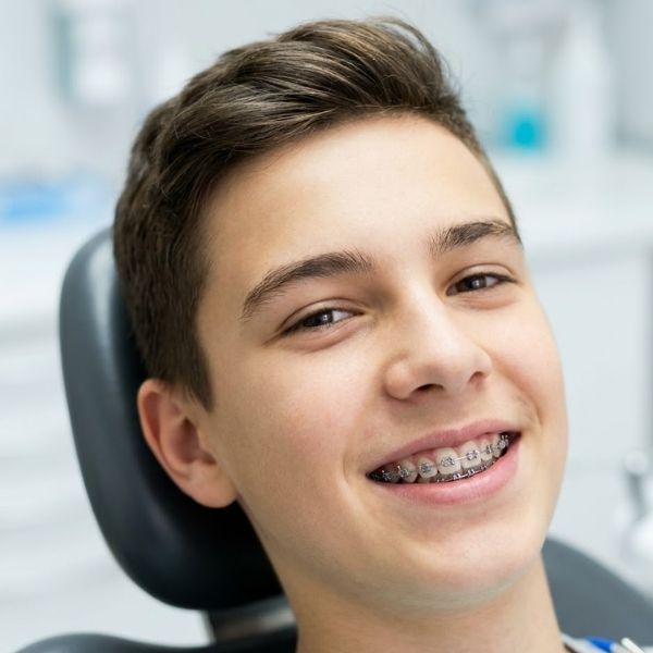 Teenage patient smiling with traditional metal braces in dental chair.